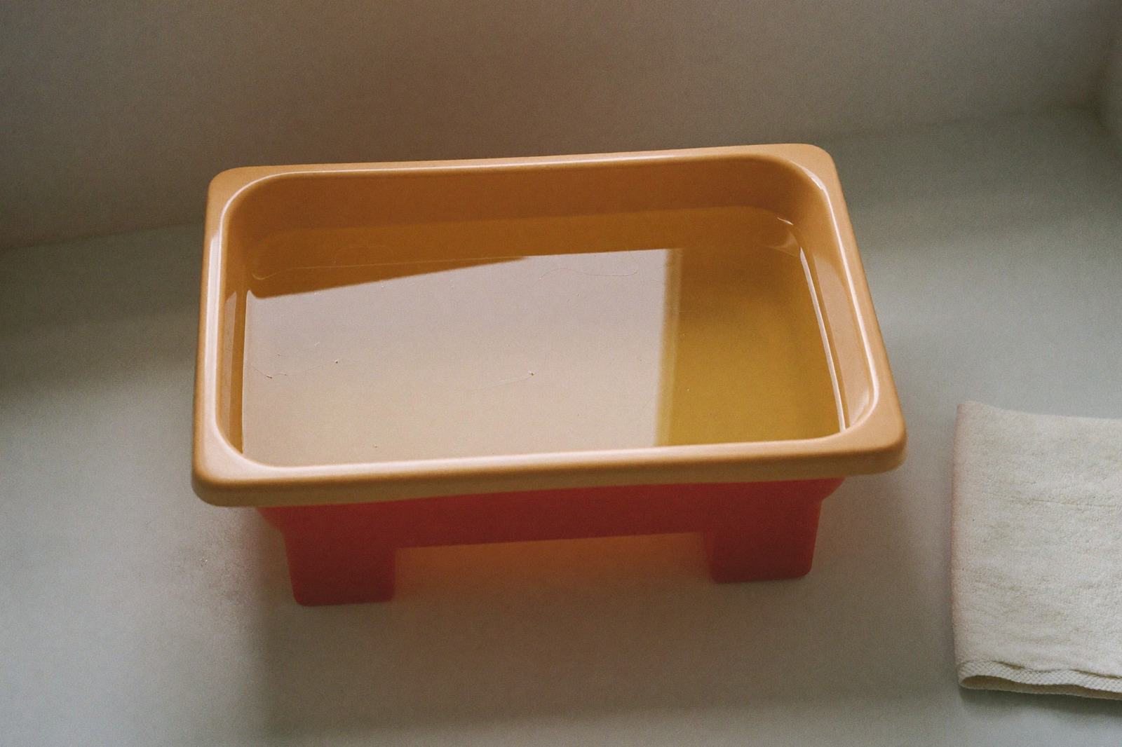 Una tina de plástico con poca agua sobre una superficie firme, junto a una toalla doblada, en un baño de luz suave
