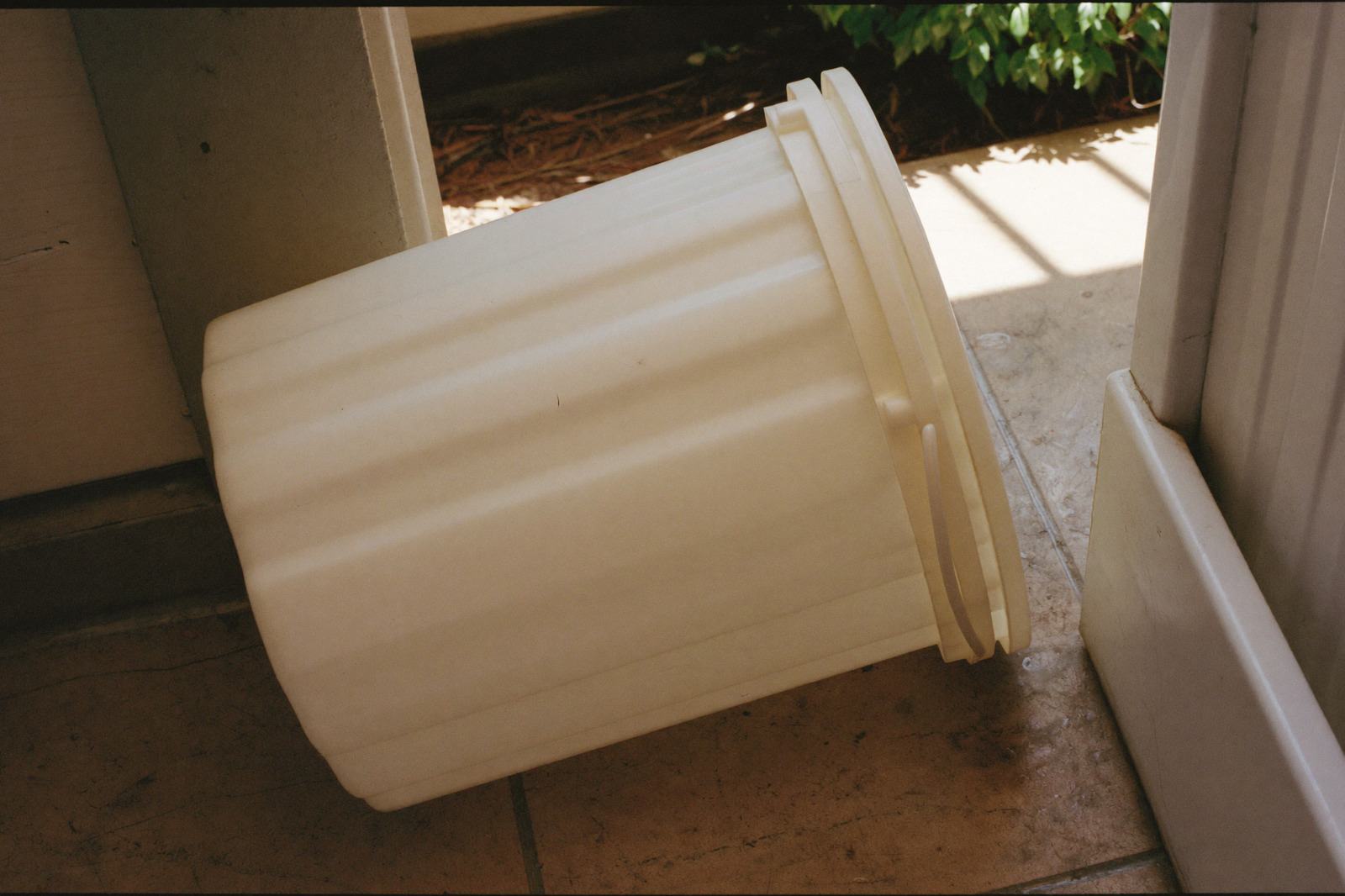 Cubeta vacía volteada de lado junto a la puerta del patio de servicio, sin agua adentro
