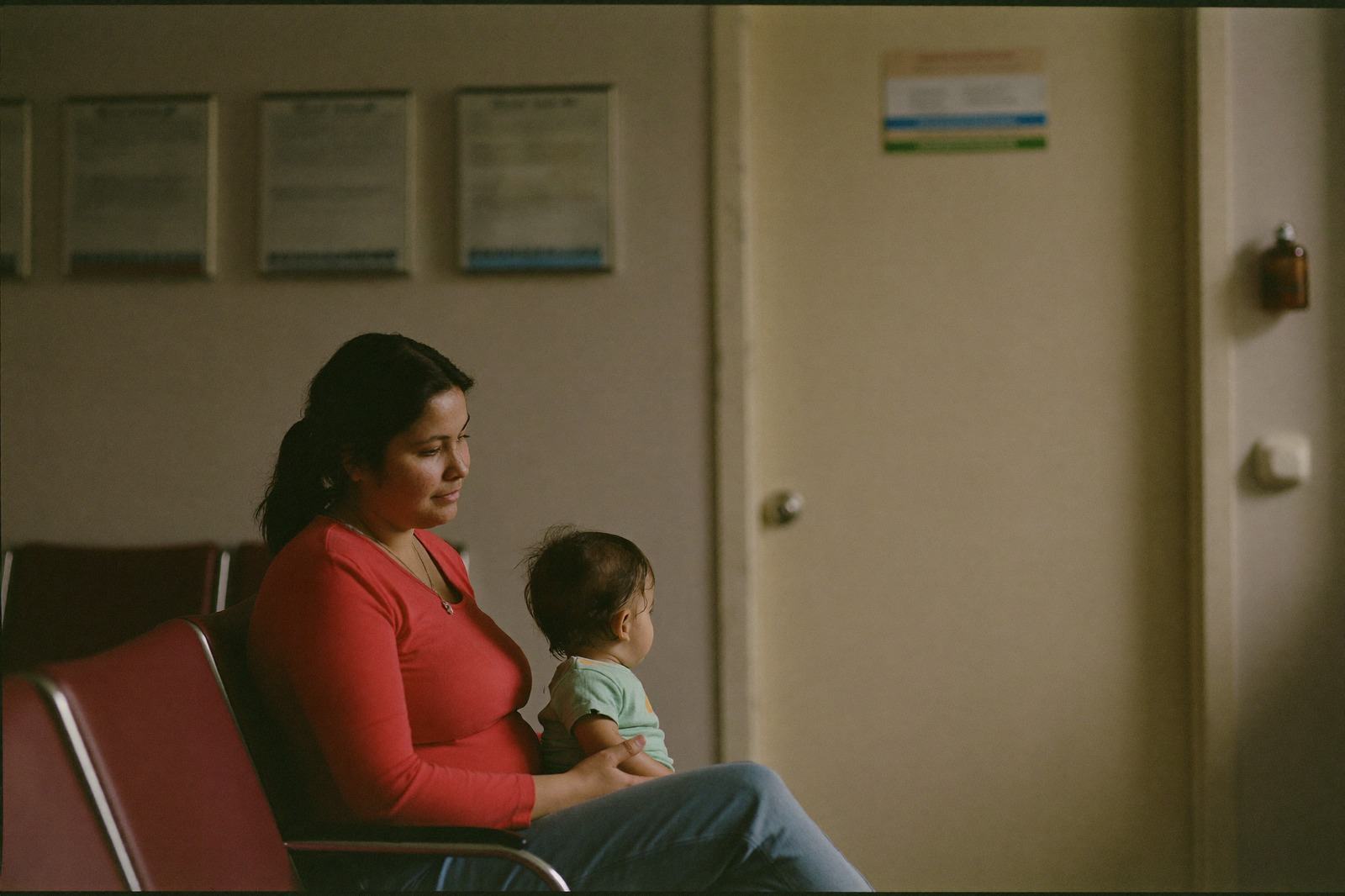 Una madre con su hijo pequeño en brazos en la sala de espera de un consultorio, mirando hacia la puerta
