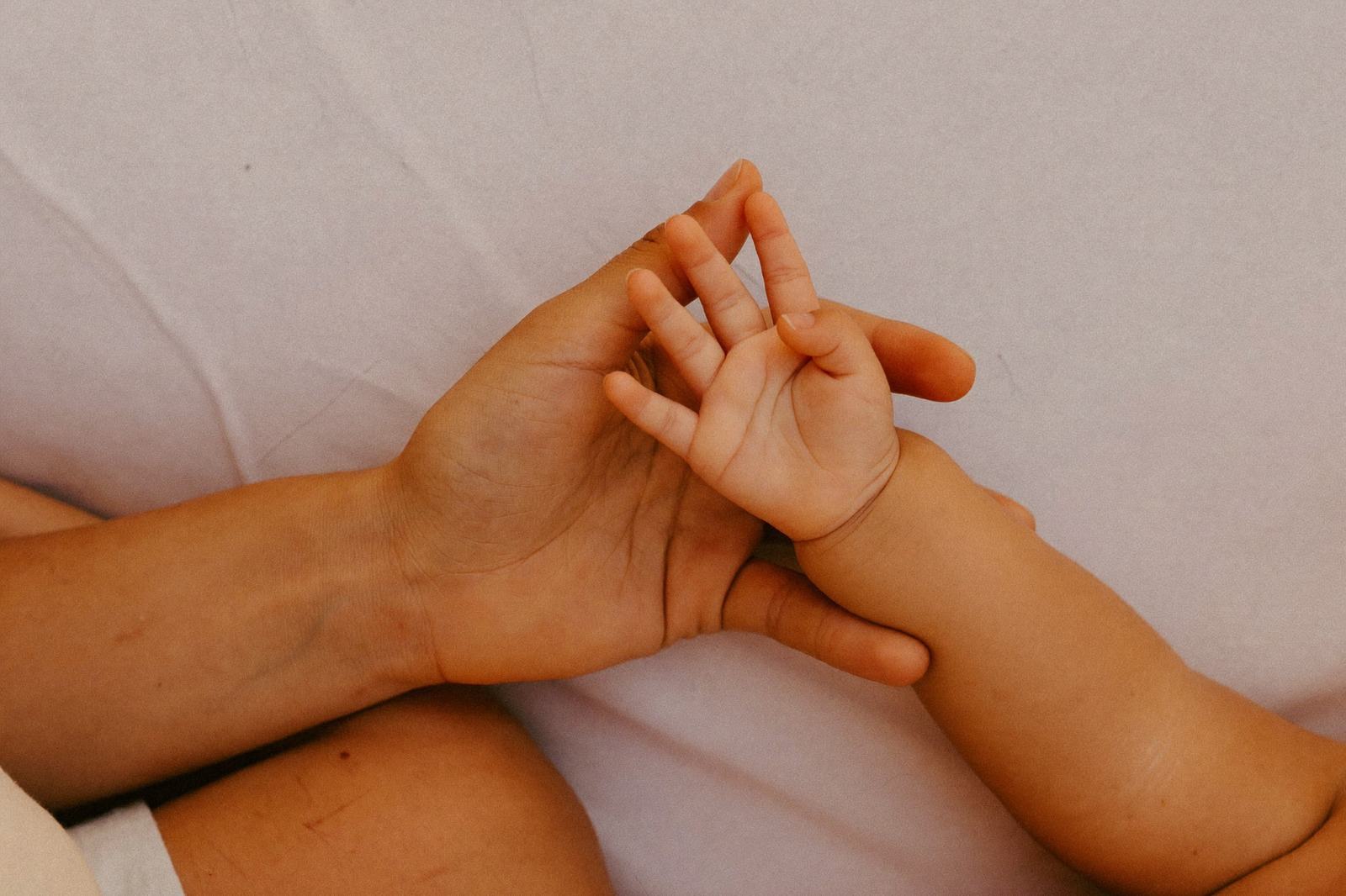 Brazo de un bebé sobre una manta clara, con la mano de un adulto revisando la piel