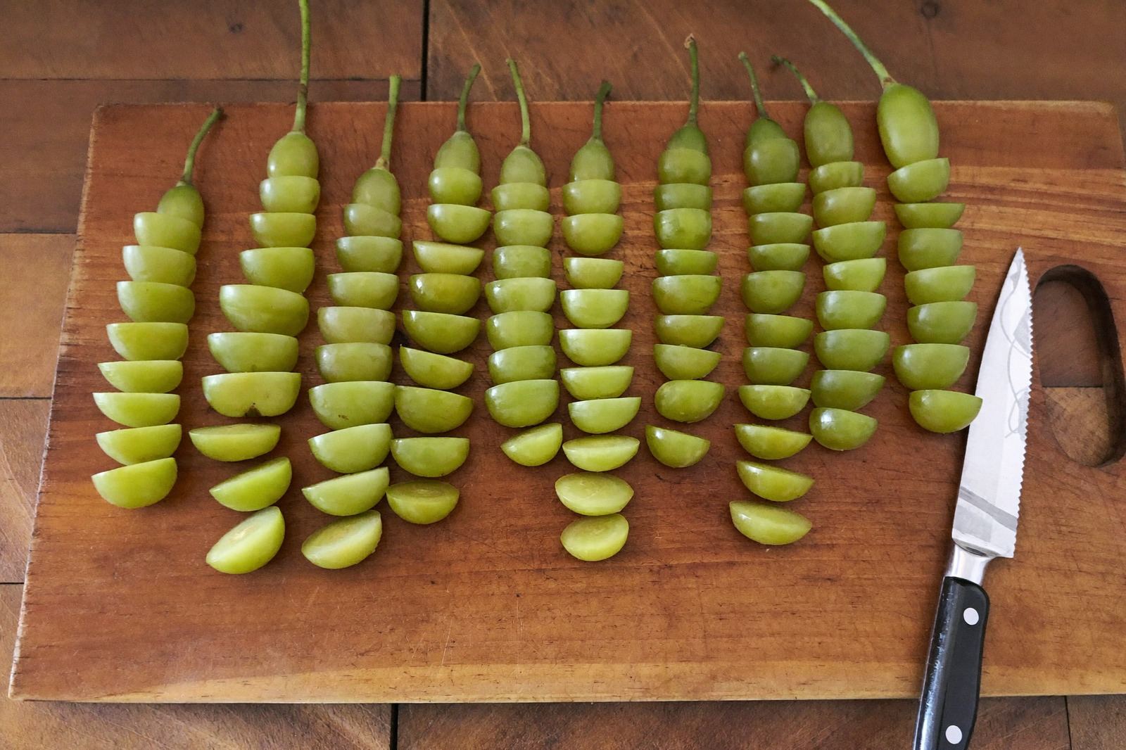 Tabla de madera con uvas partidas a lo largo en cuartos junto a un cuchillo pequeño