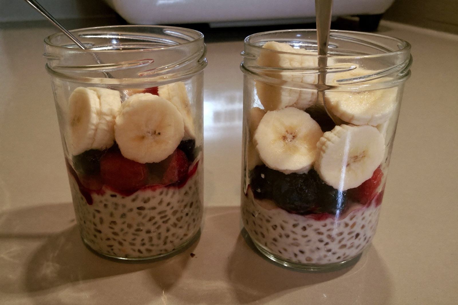Dos frascos de vidrio con avena remojada y fruta encima, listos en la barra de la cocina