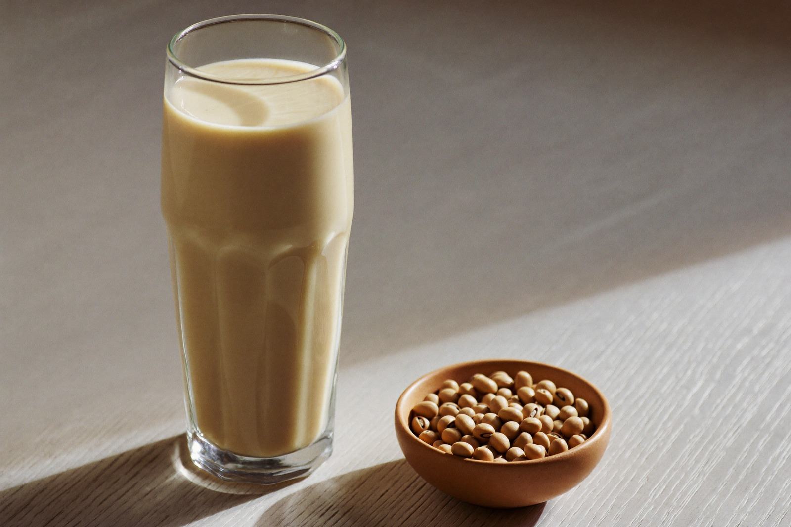 Vaso de bebida de soya servido junto a un tazón con soya en grano sobre una mesa de madera clara