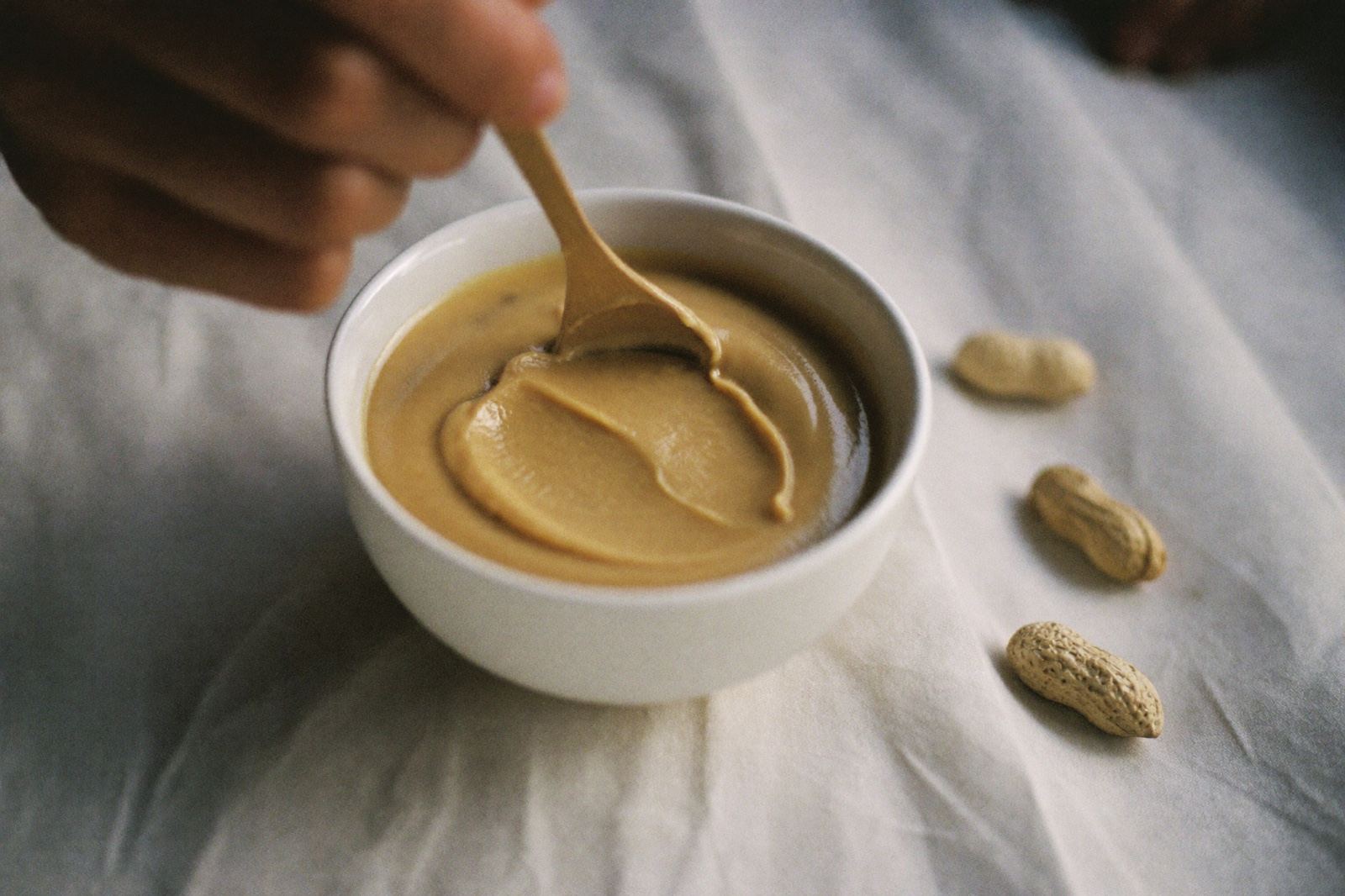 Un tazón pequeño de puré de fruta con crema de cacahuate disolviéndose dentro, revuelta con una cuchara de madera para bebé