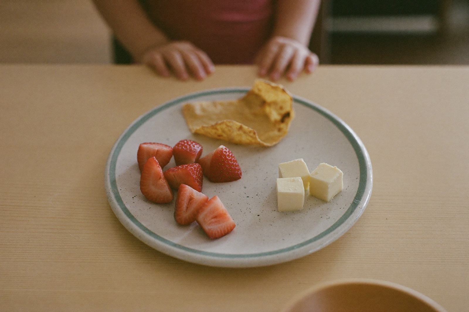 Plato pequeño con fresas en cuartos, cubos de queso y un trozo de tortilla sobre una mesa de madera