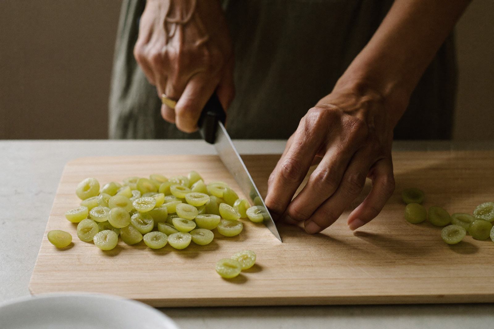 Manos cortando uvas a lo largo sobre una tabla de madera clara junto a un plato pequeño