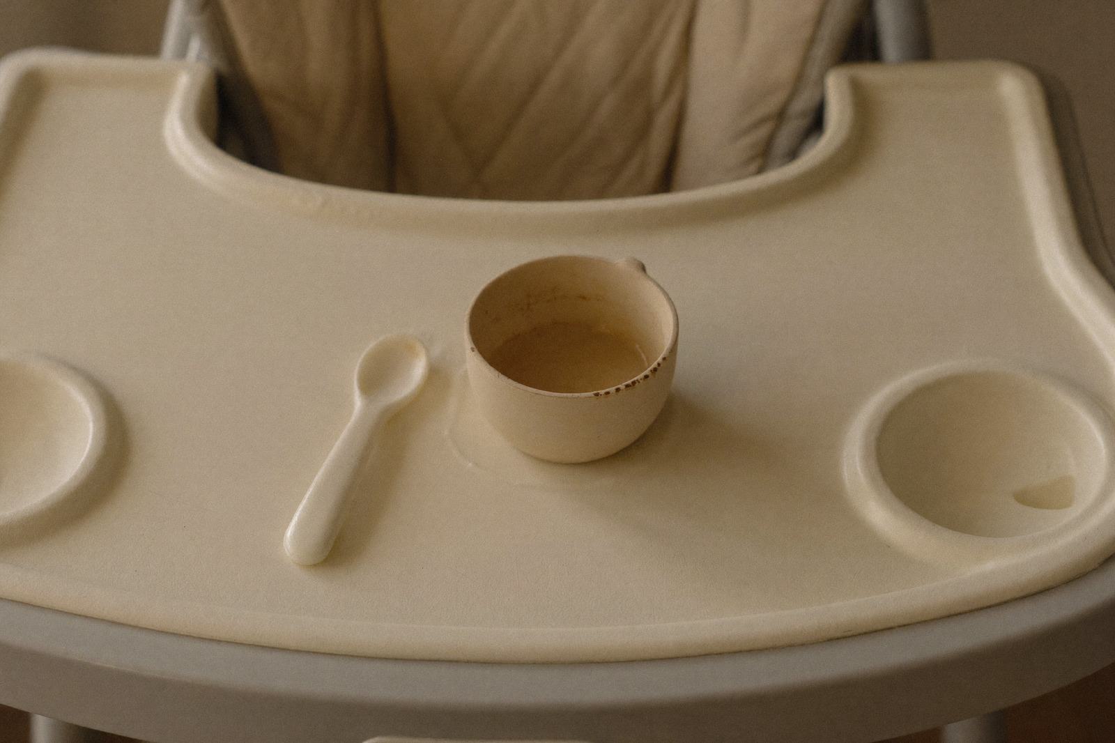 Vaso pequeño sin tapa y cuchara de bebé sobre la bandeja de una silla alta