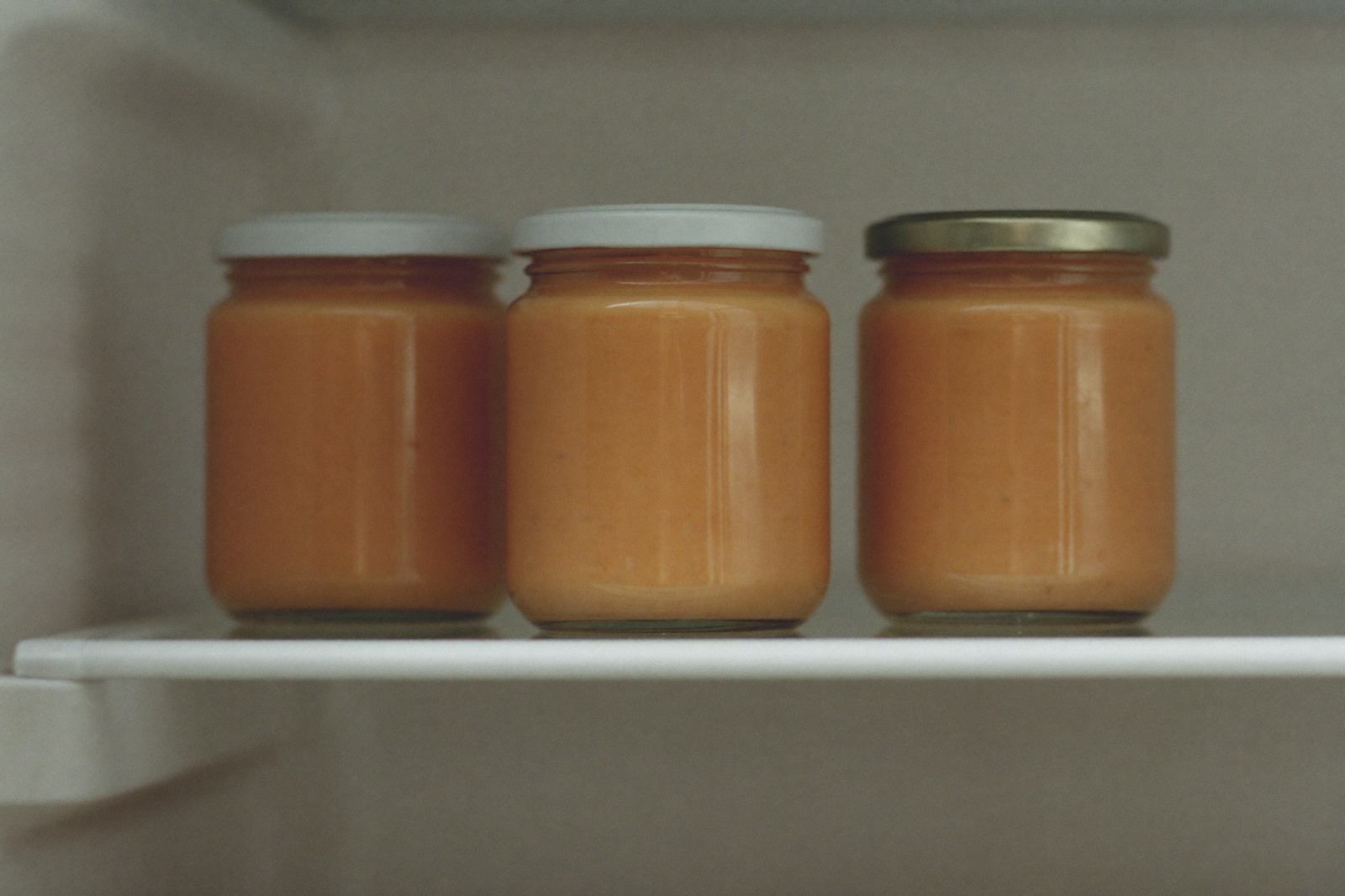 Frascos pequeños de vidrio con puré casero, tapados, sobre la charola del refrigerador