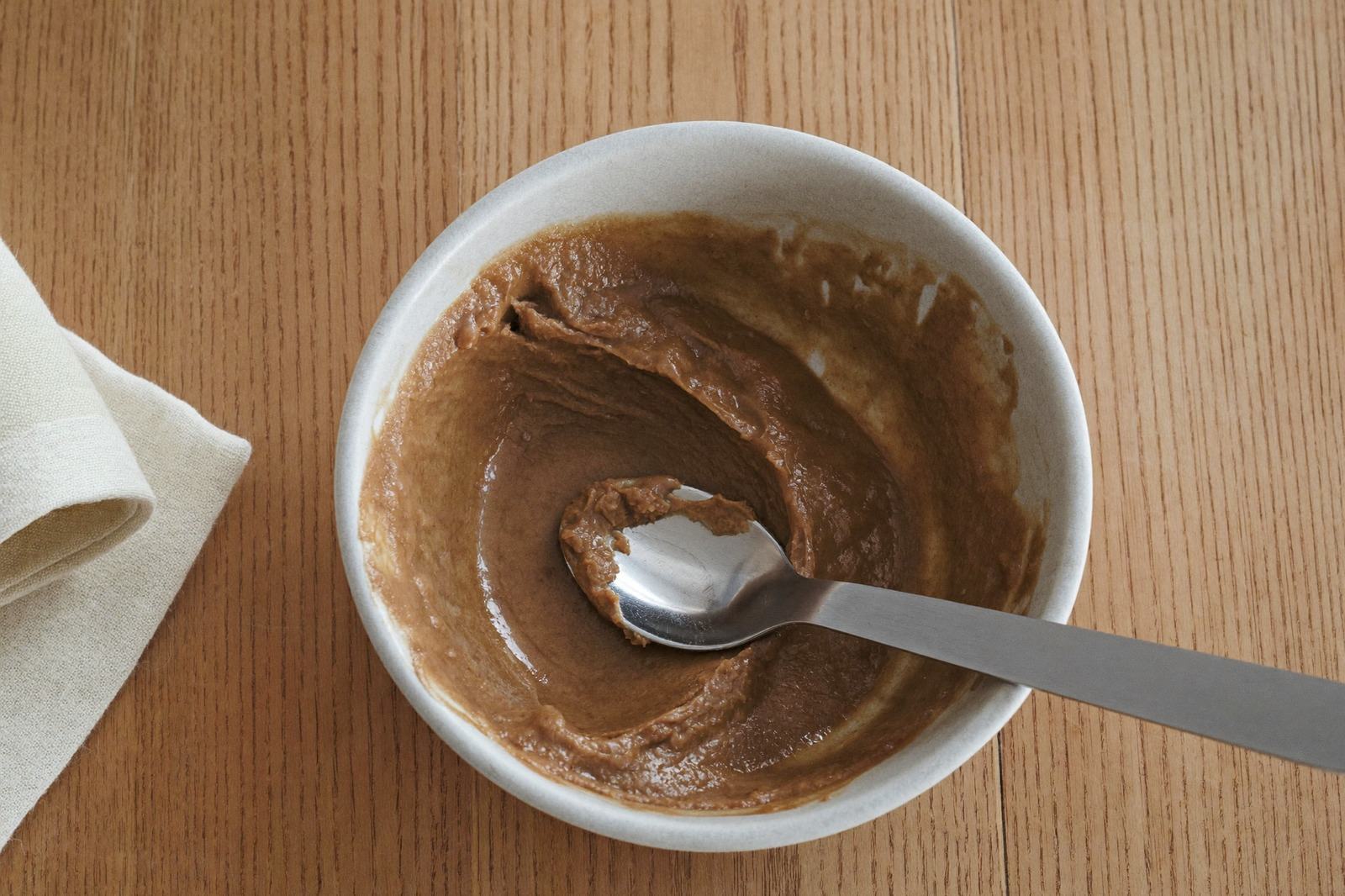 Cuchara con frijoles machacados sobre un tazón pequeño de cerámica junto a una servilleta de tela