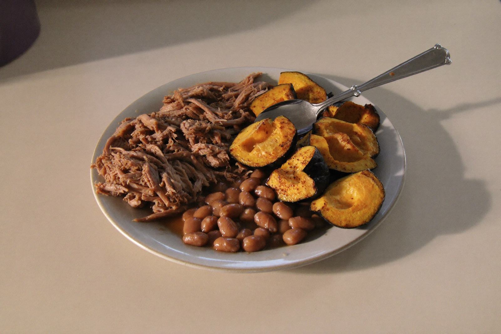 Plato hondo con carne deshebrada, frijoles machacados y calabaza cocida sobre una mesa clara