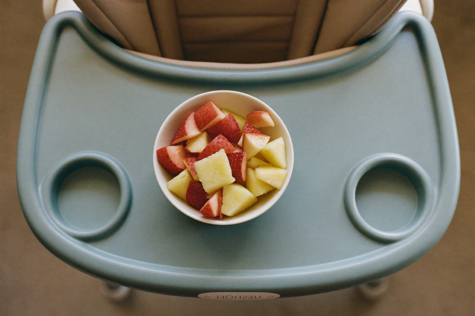 Tazón pequeño con fruta cortada en trozos blandos sobre la bandeja de una silla alta