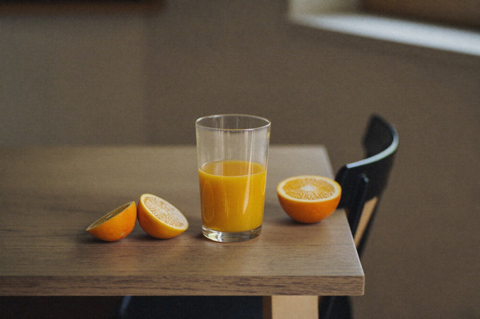 Vaso pequeño con jugo de naranja junto a naranjas partidas sobre una mesa de madera clara