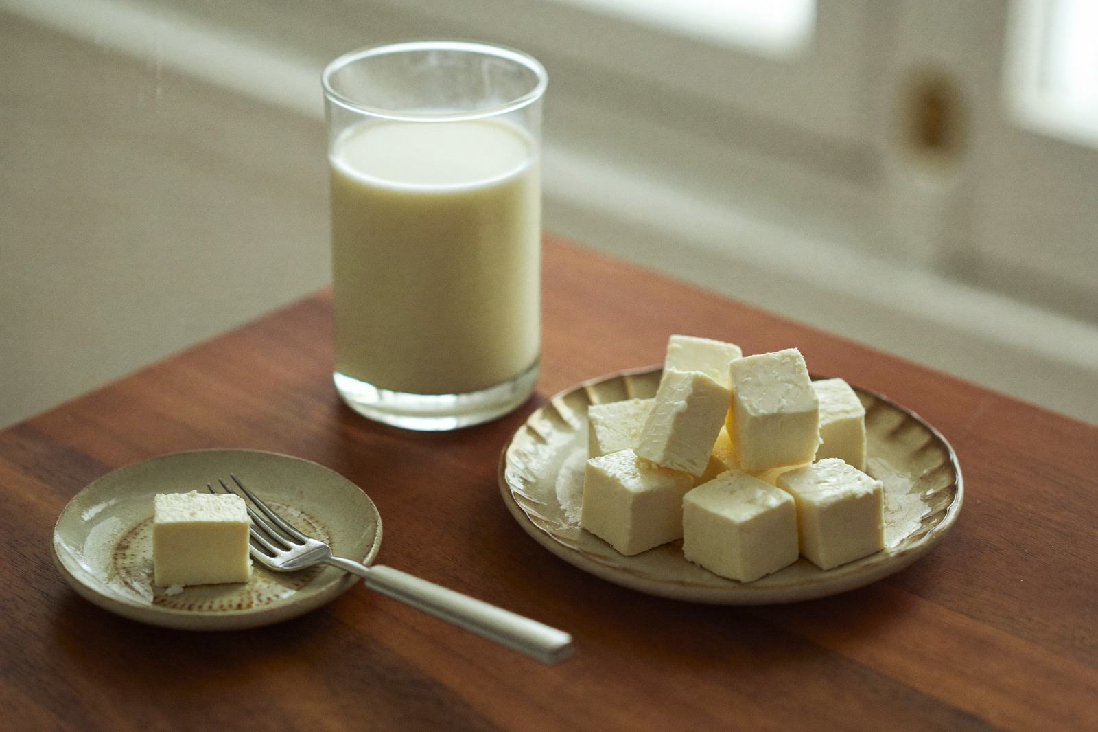 Vaso de leche servido sobre una mesa de madera junto a un plato con queso en cubos