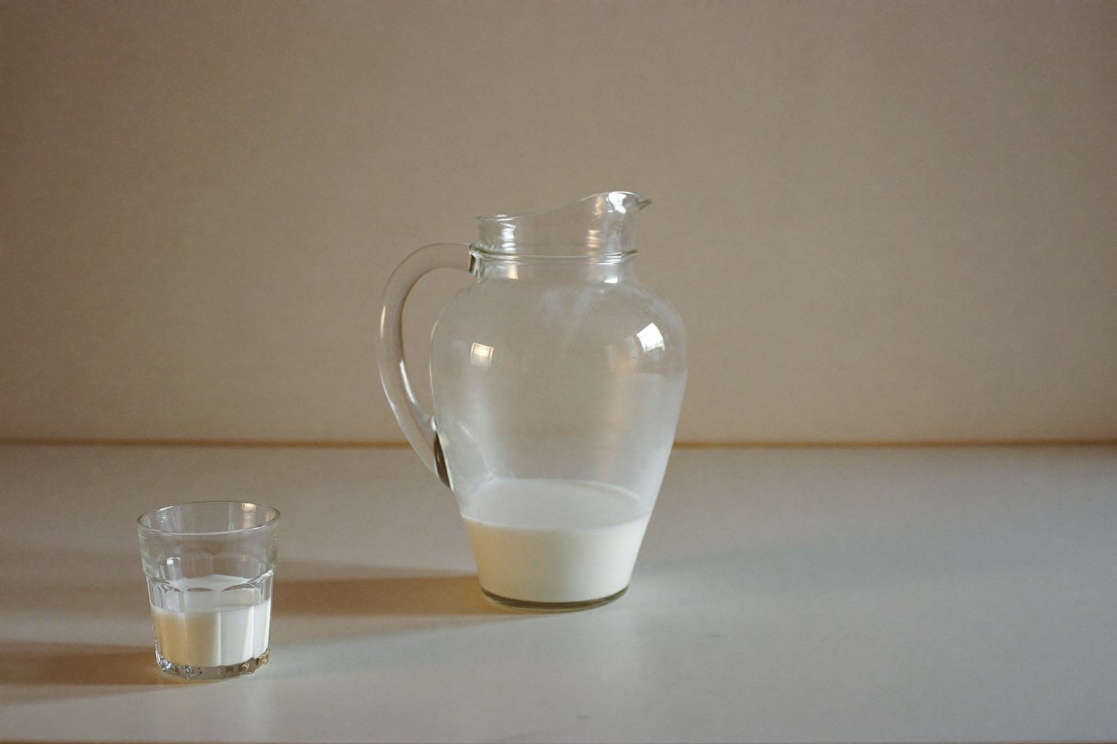 Jarra de vidrio con leche y un vaso servido sobre la barra de una cocina luminosa