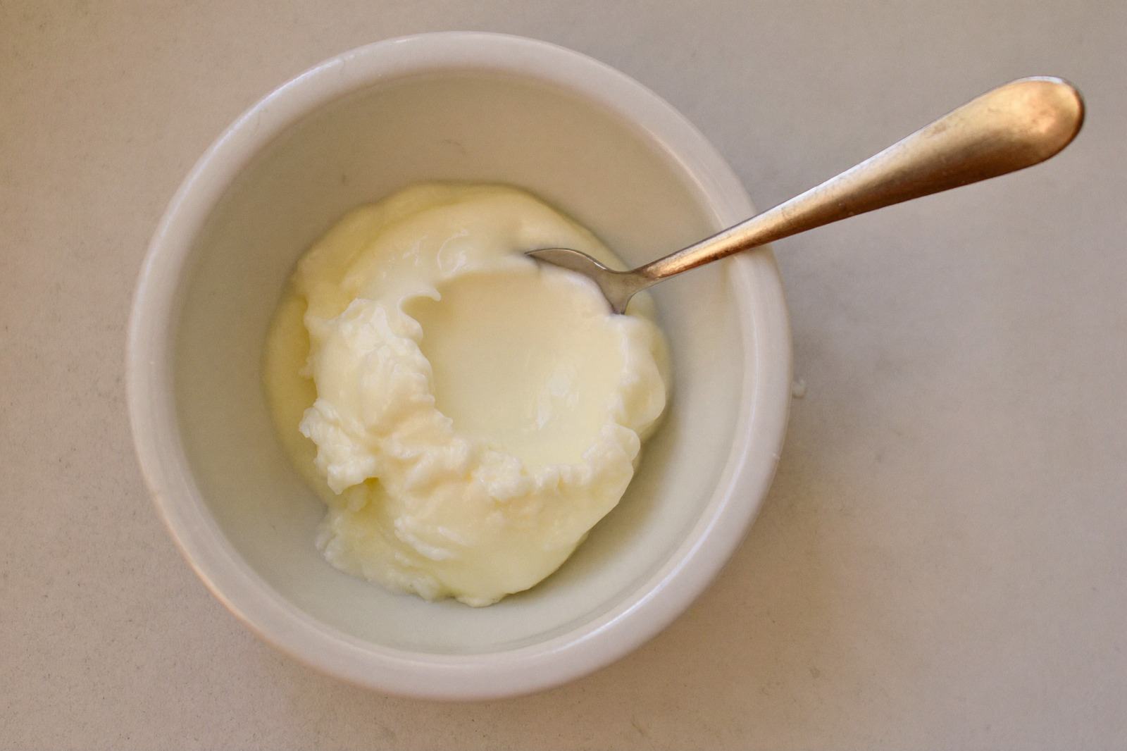 Tazón pequeño con yogur natural y una cuchara de bebé sobre una superficie clara