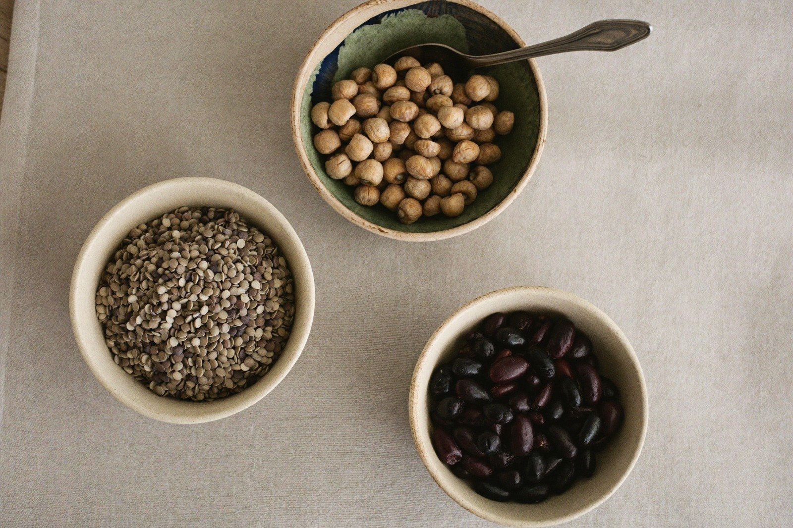 Tazones pequeños con lentejas, garbanzos y frijoles crudos sobre una superficie de madera