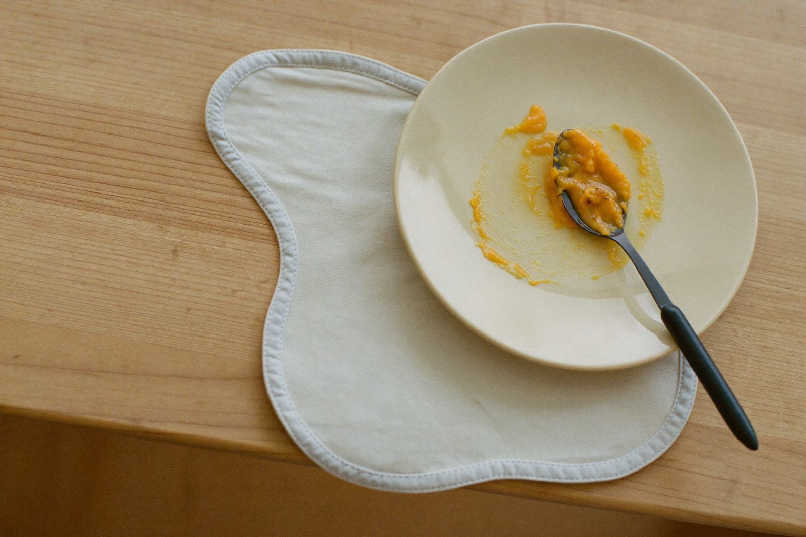 Cuchara pequeña con puré de color naranja apoyada sobre un plato blanco junto a un babero de lino