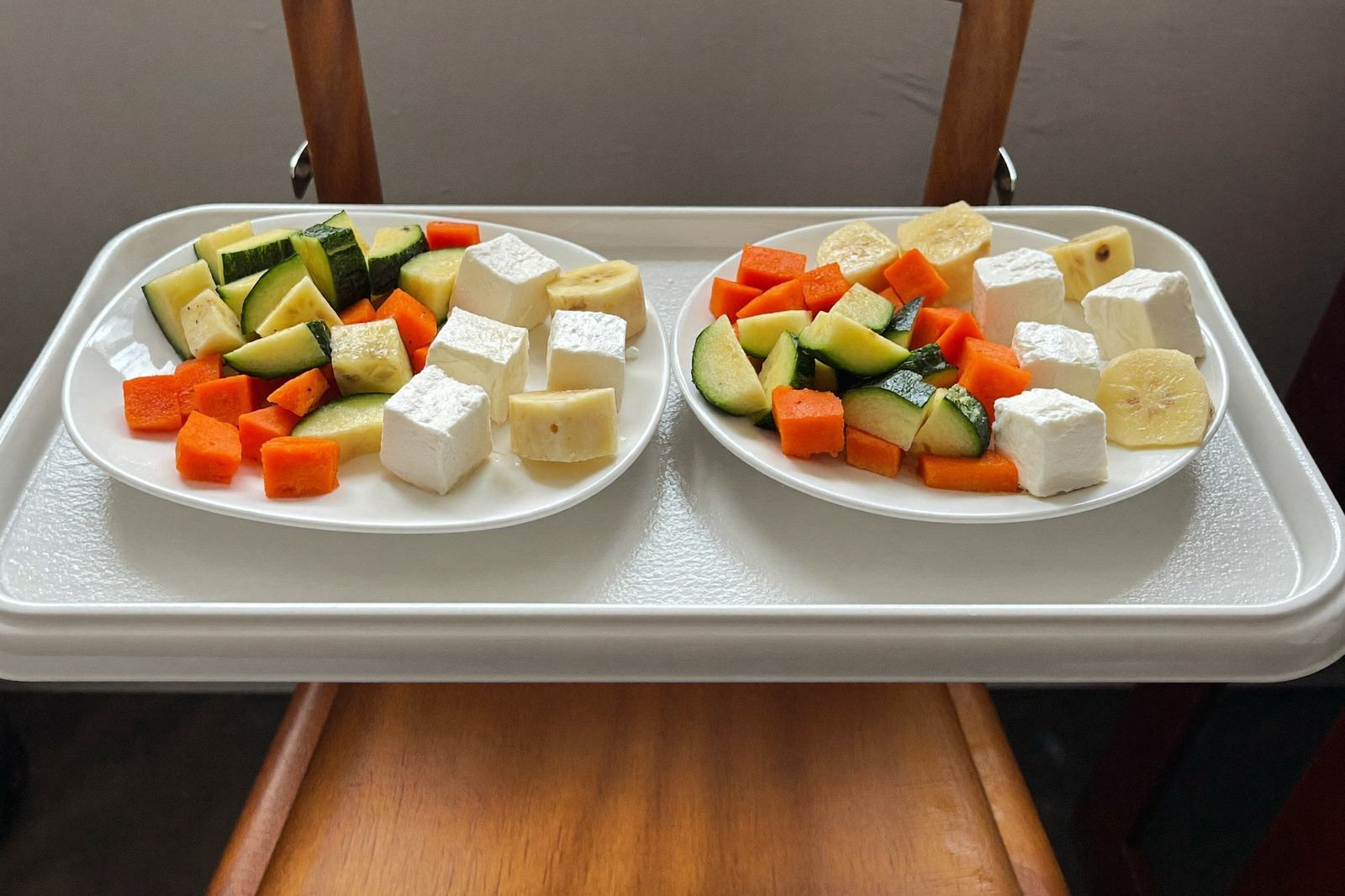 Plato de bebé con verduras en cubos, plátano y trocitos de queso sobre la charola de una periquera