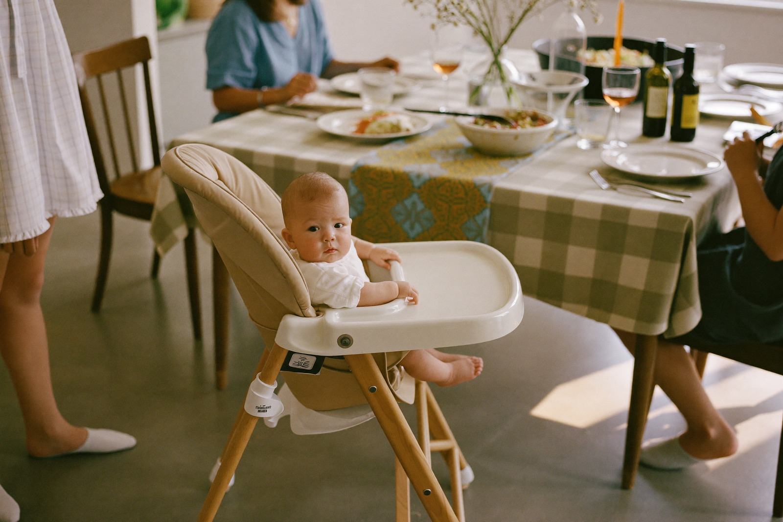Mesa familiar puesta para comer con un bebé en silla alta integrado a la mesa y platos de adultos alrededor