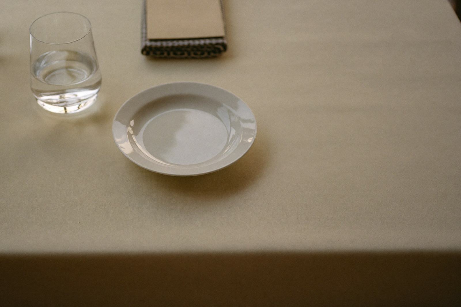 Mesa de restaurante despejada con solo un plato pequeño y un vaso de agua sobre el mantel