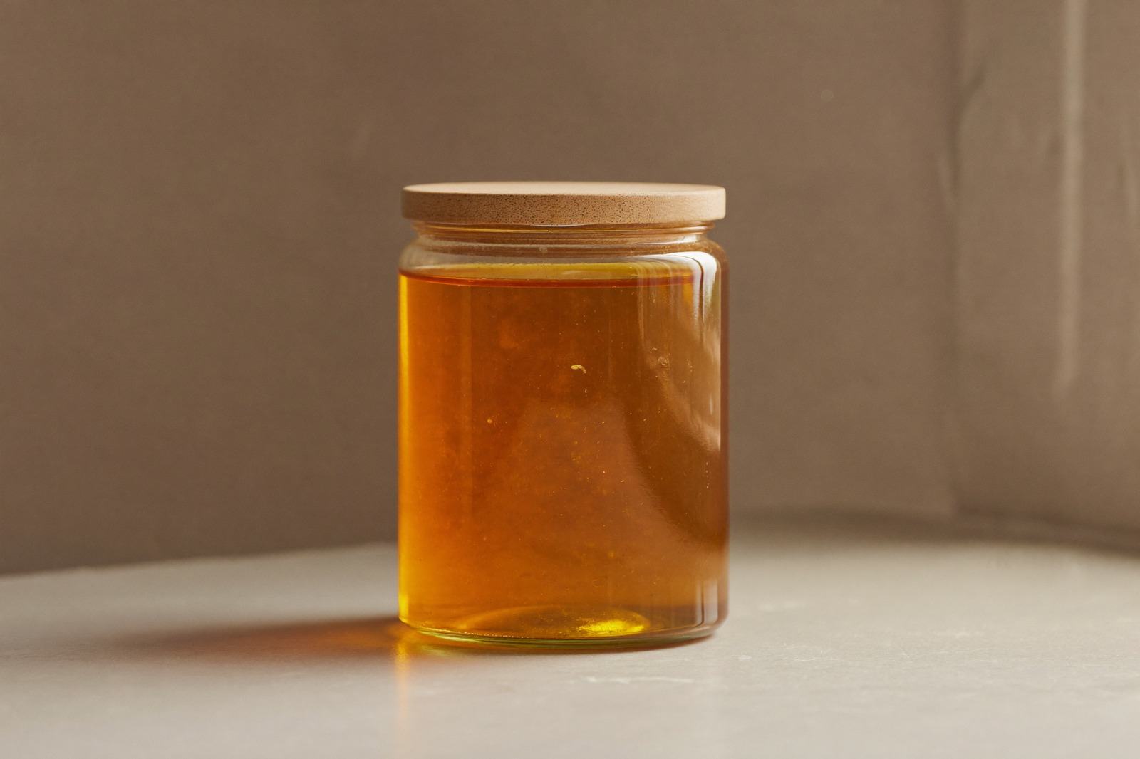 Frasco de vidrio con miel cerrado con tapa de madera sobre una superficie clara de cocina, con luz cálida de mañana