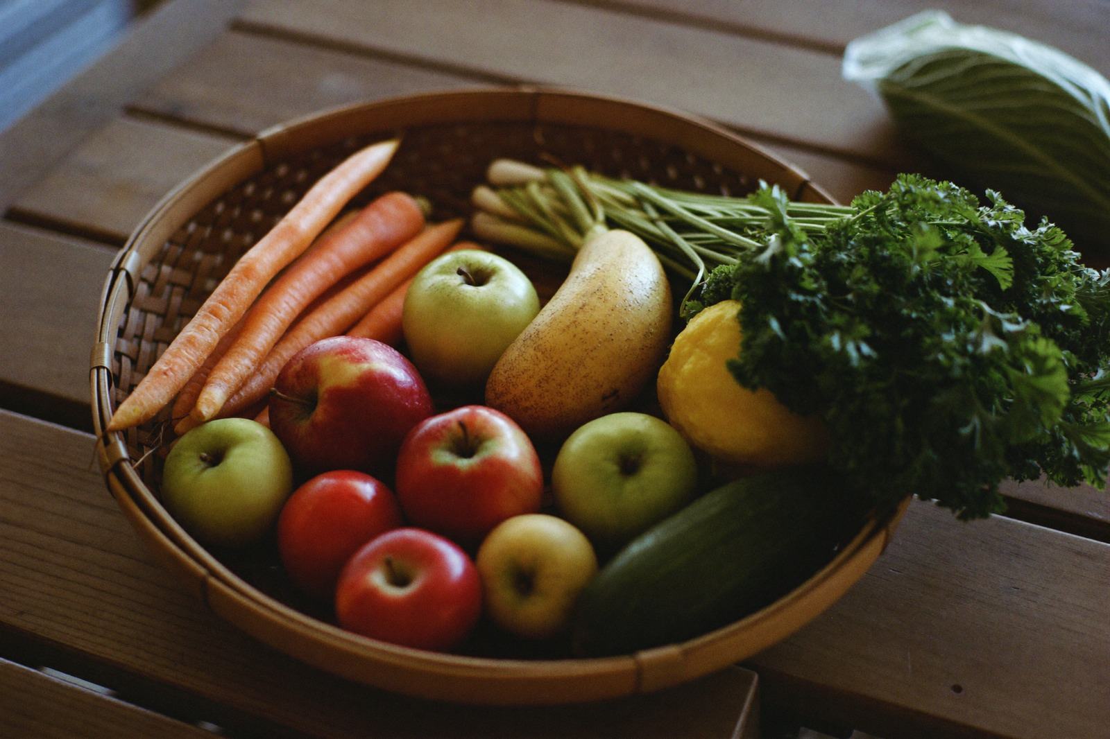 Verduras y frutas frescas sin empaque acomodadas en una canasta sobre una mesa de madera