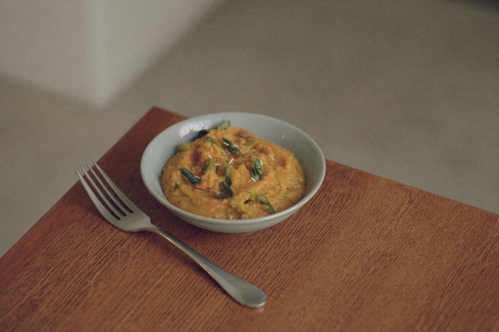 Verduras cocidas y machacadas en un tazón sobre una mesa de madera, con un tenedor apoyado al lado