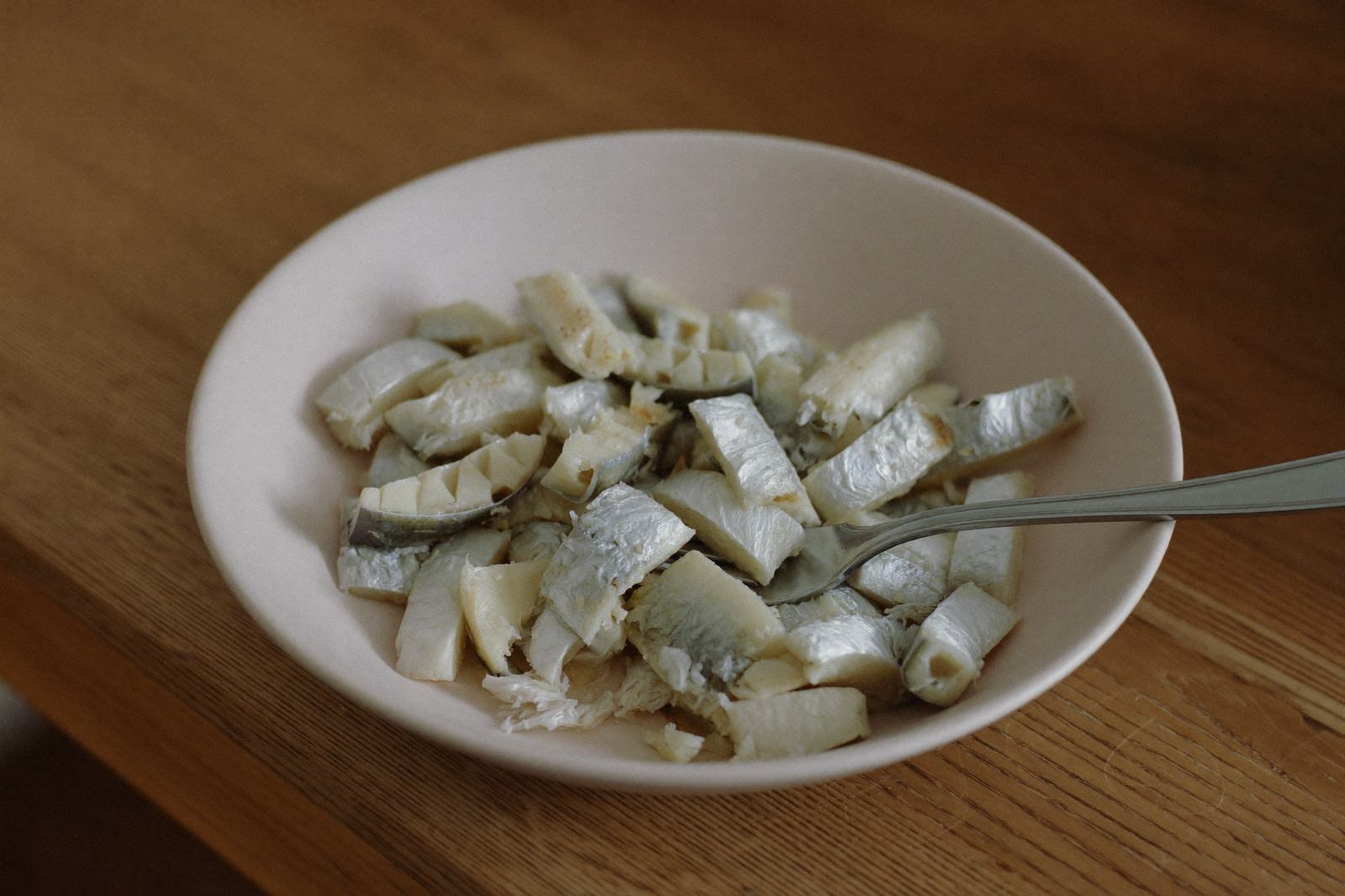Pescado cocido desmenuzado en trozos pequeños en un tazón blanco, con un tenedor apoyado encima