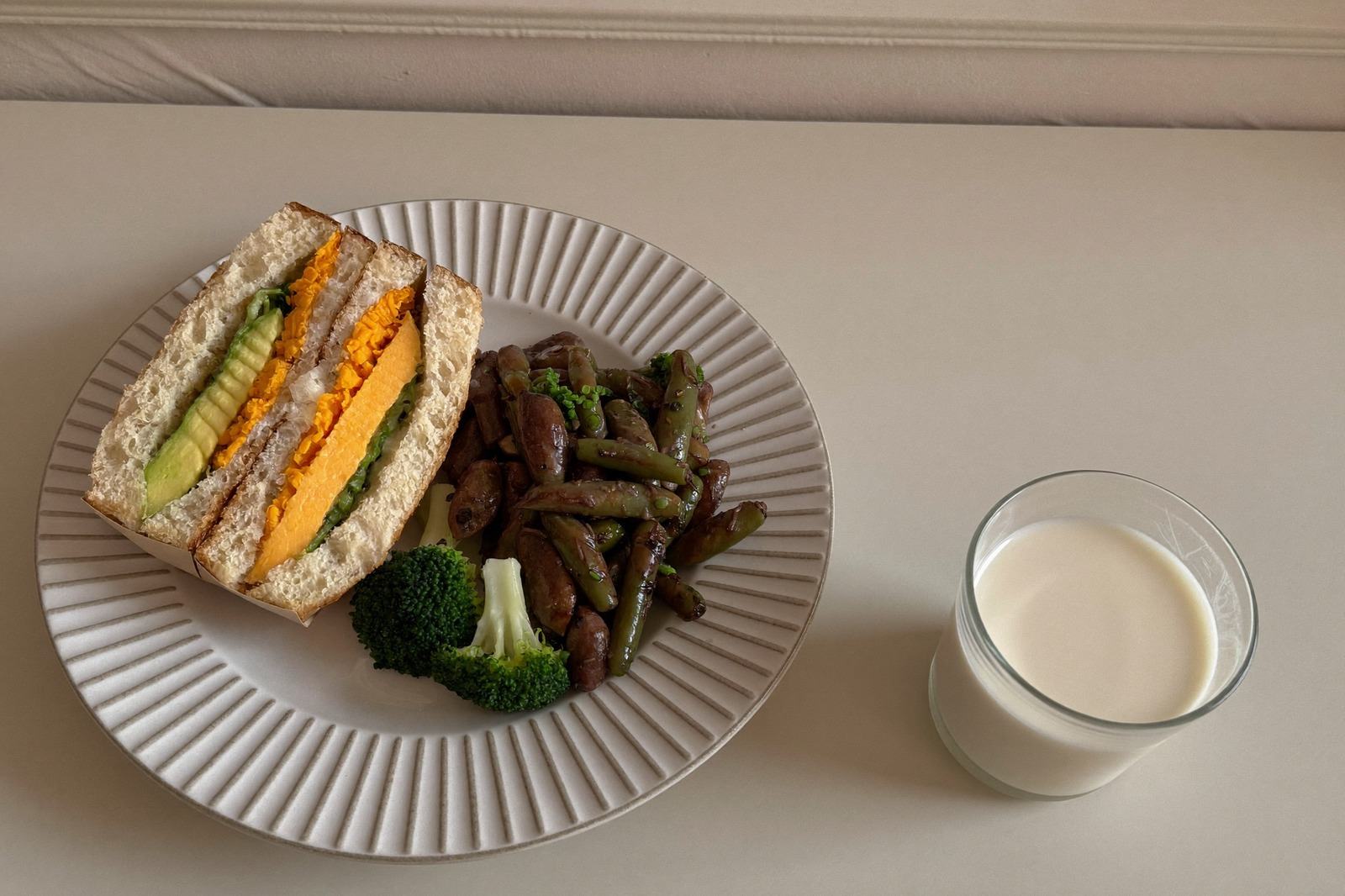 Plato pequeño con medio sándwich cortado, verduras verdes cocidas y un vaso de leche