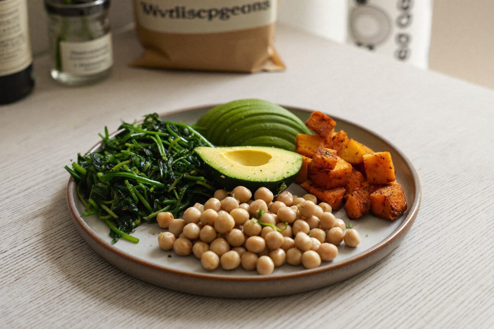 Plato con verduras de colores, garbanzos y aguacate sobre una mesa de madera clara