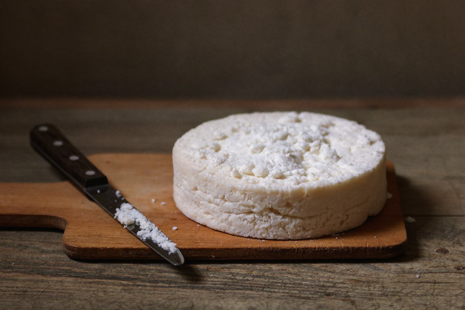 Rueda de queso fresco blanco sobre una tabla de madera junto a un cuchillo