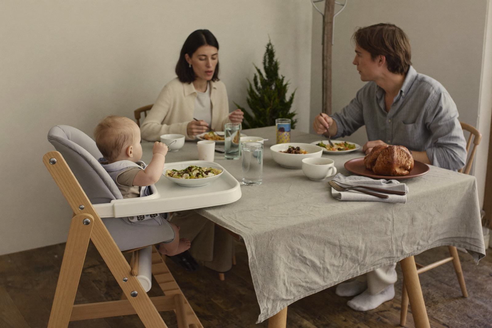 Mesa familiar con un bebé en silla alta comiendo junto a dos adultos que también comen