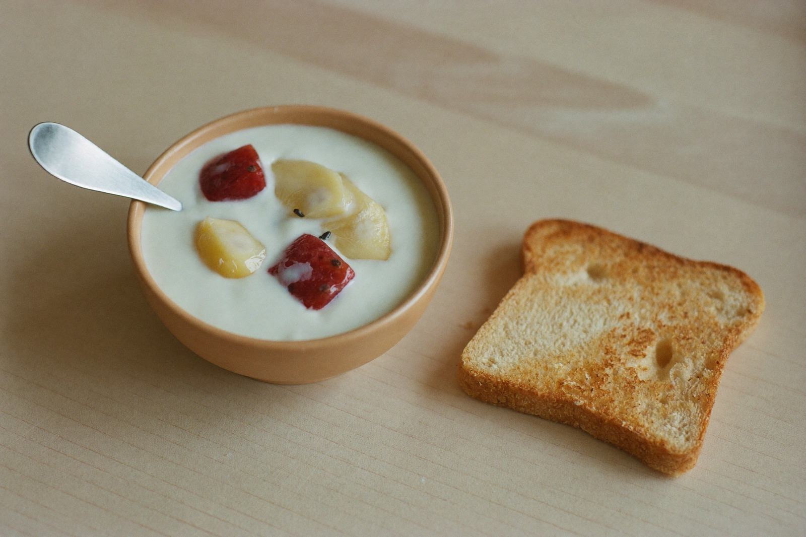 Tazón pequeño con yogur natural y fruta en cubos junto a una tostada partida