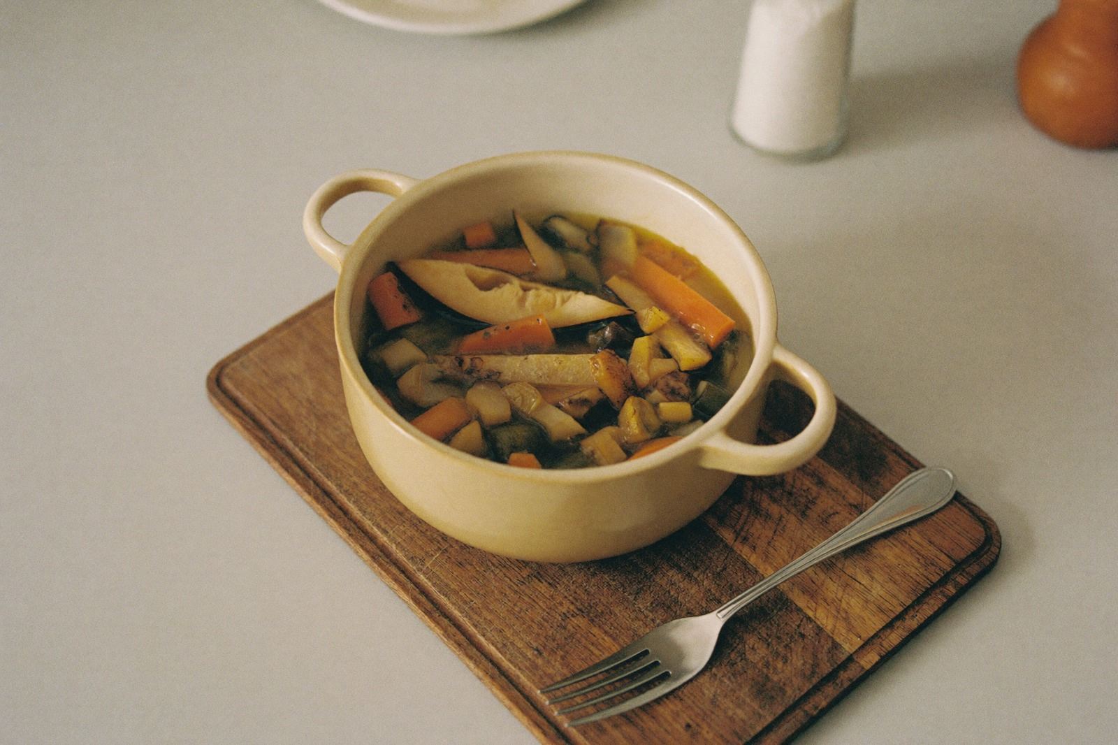 Olla pequeña con verdura cocida y un tenedor apoyado sobre una tabla de madera, sin condimentos a la vista