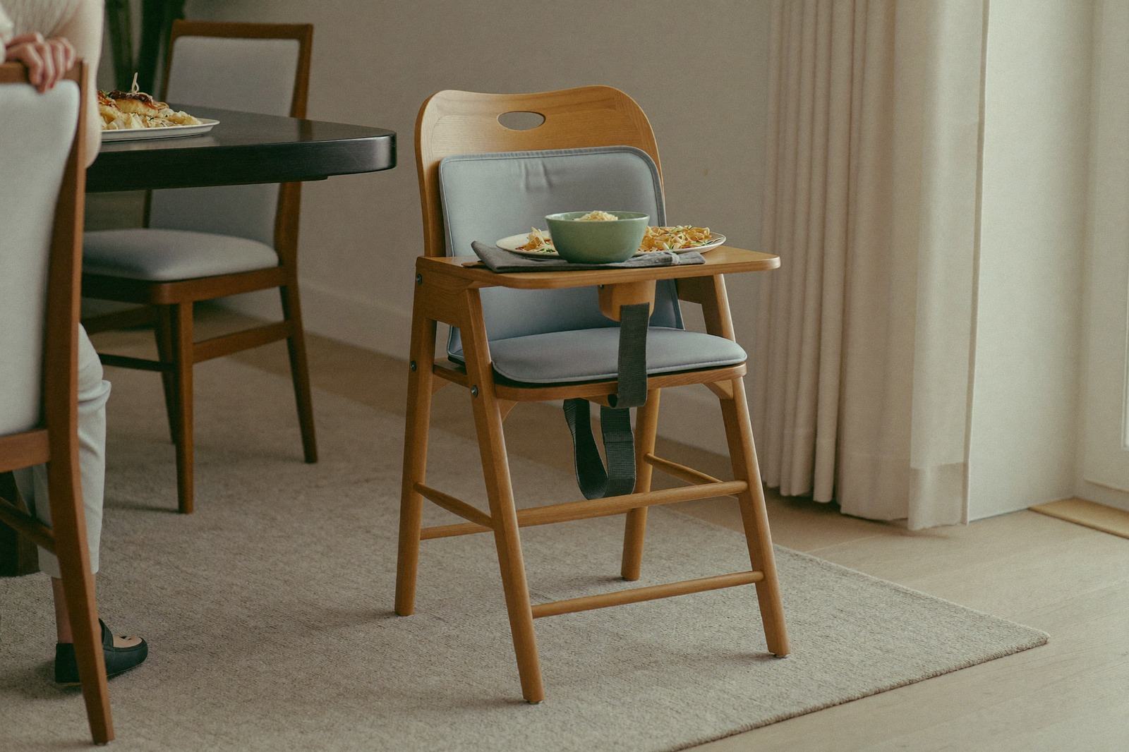 Silla alta de madera con su bandeja y un tazón con comida cortada, junto a una mesa familiar