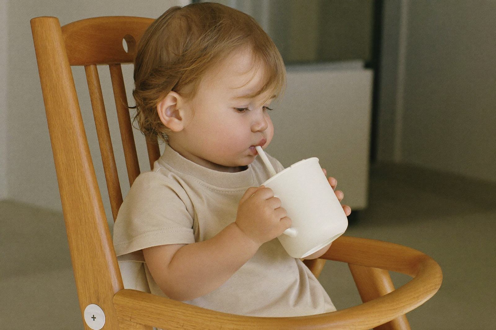 Bebé sentado a la mesa sosteniendo con las dos manos un vaso pequeño de agua