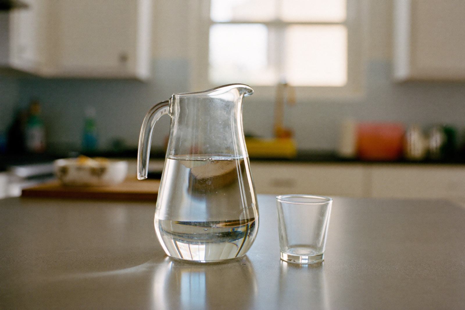 Jarra de vidrio con agua y un vaso pequeño sobre la barra de una cocina con luz de mañana