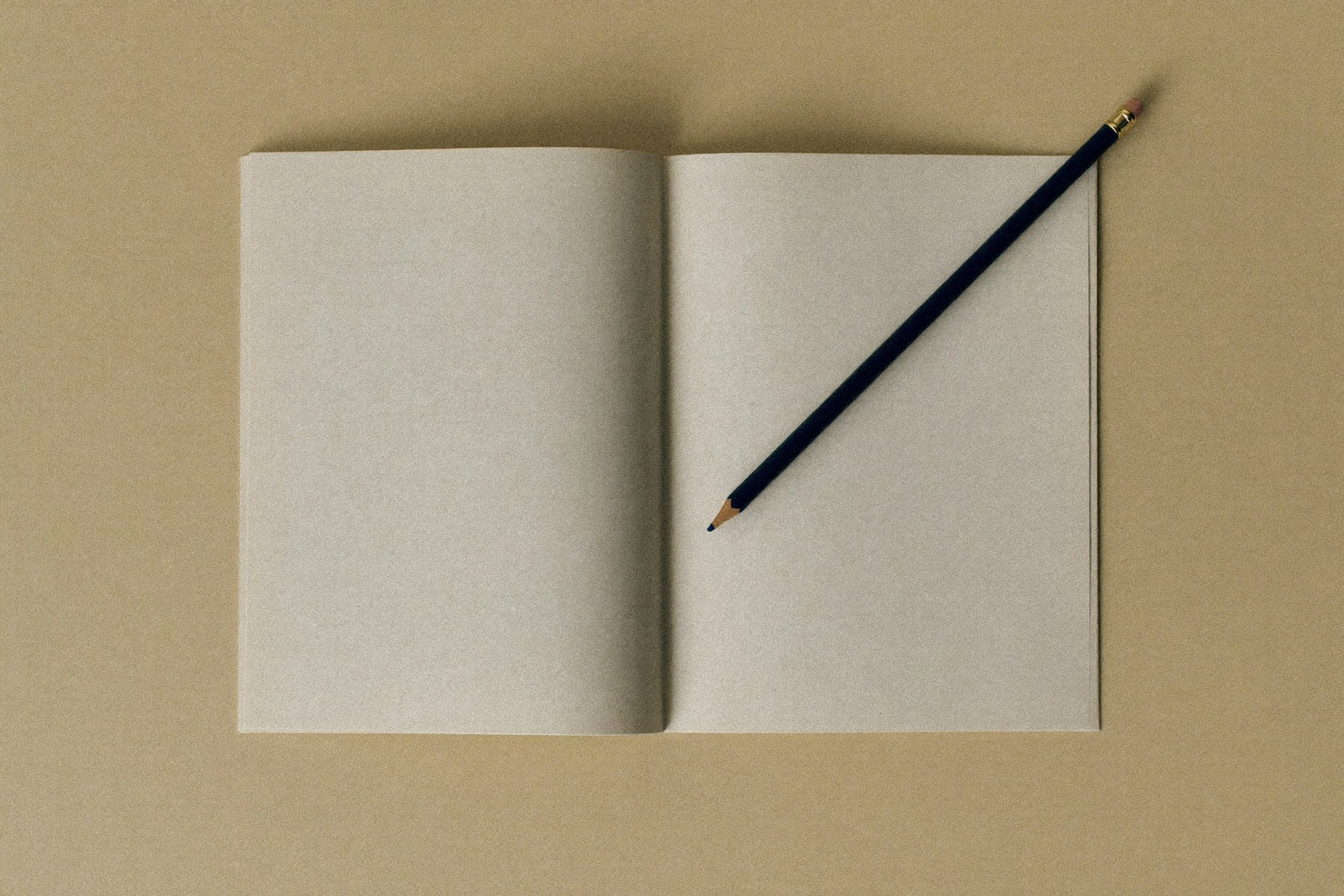 Una libreta de páginas en blanco abierta sobre una mesa, con un lápiz azul marino apoyado en diagonal
