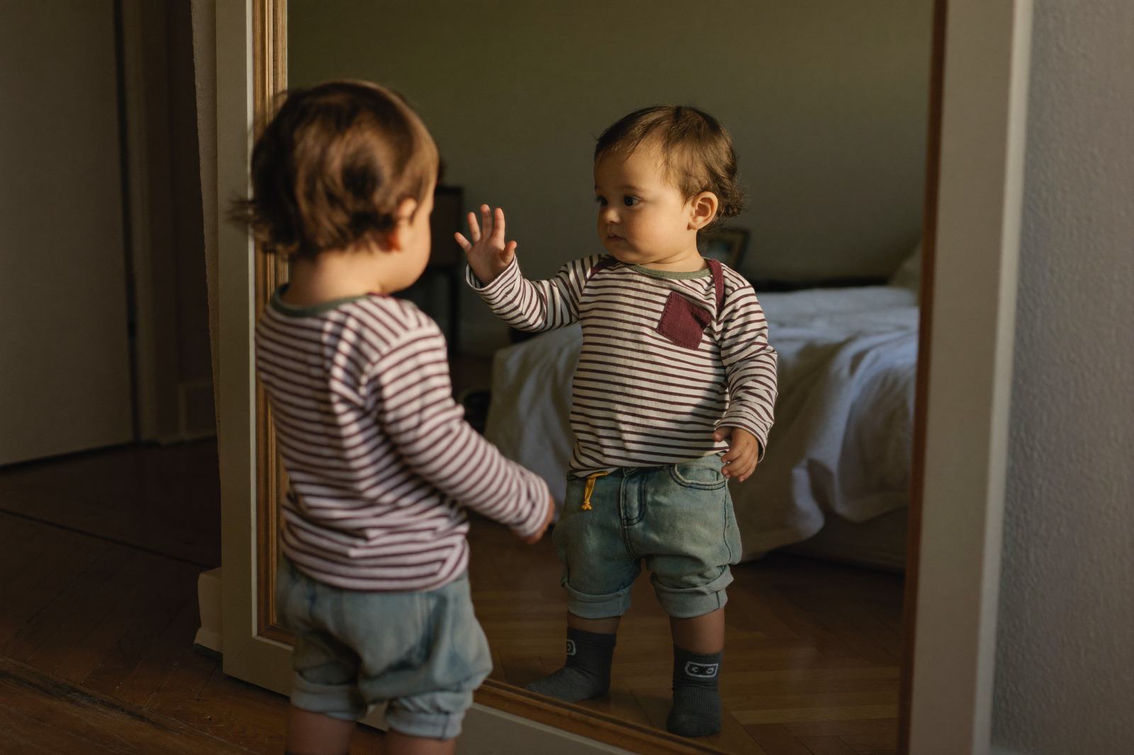 Niño pequeño de espaldas frente a un espejo de cuerpo entero en una habitación luminosa