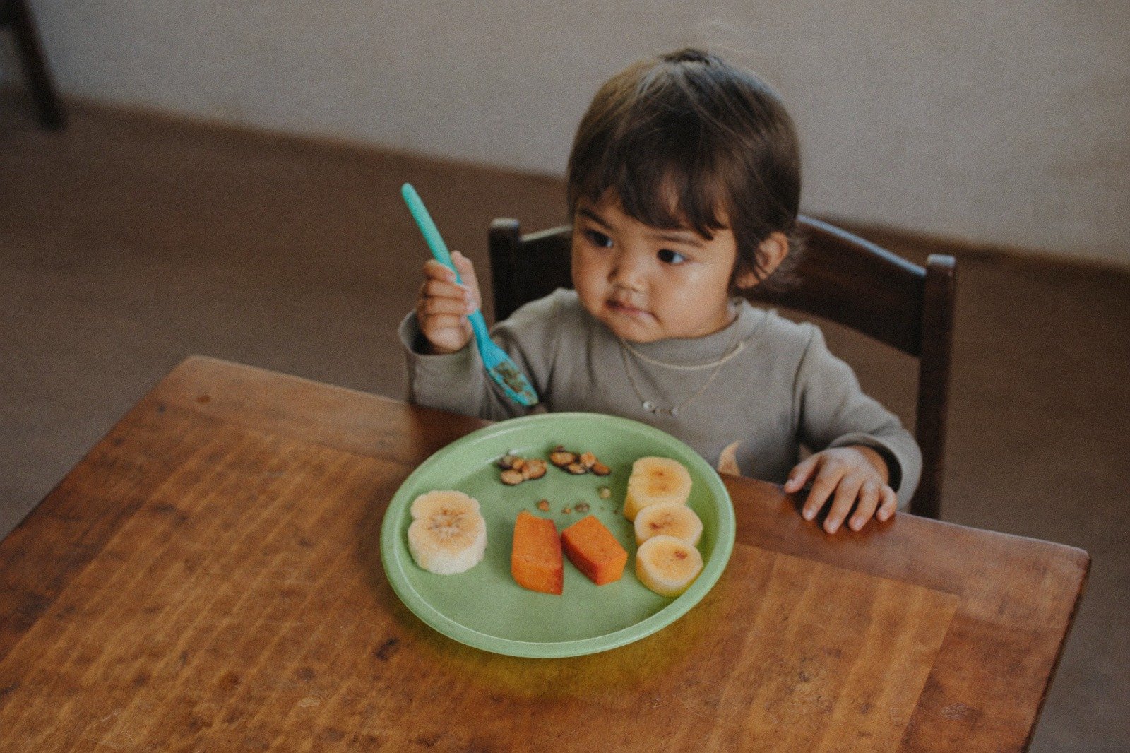 Plato infantil con porciones pequeñas de fruta y verdura sobre una mesa de madera