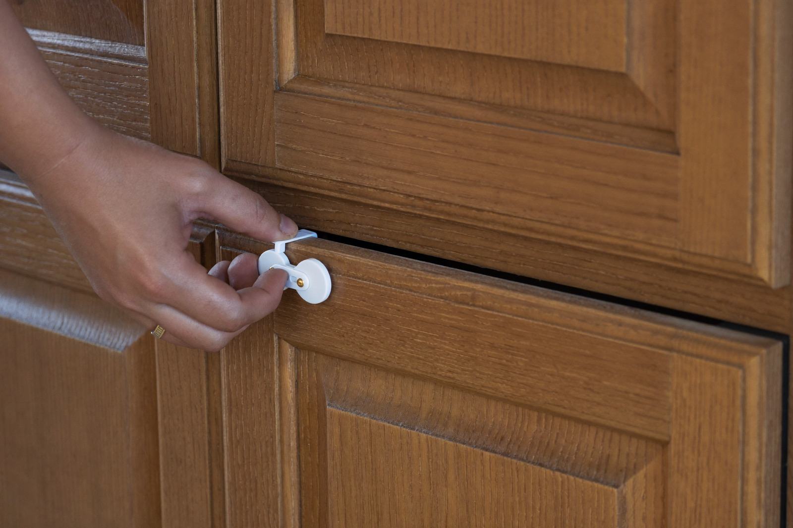 Puerta de alacena de madera con un pestillo de seguridad instalado, y una mano soltándolo
