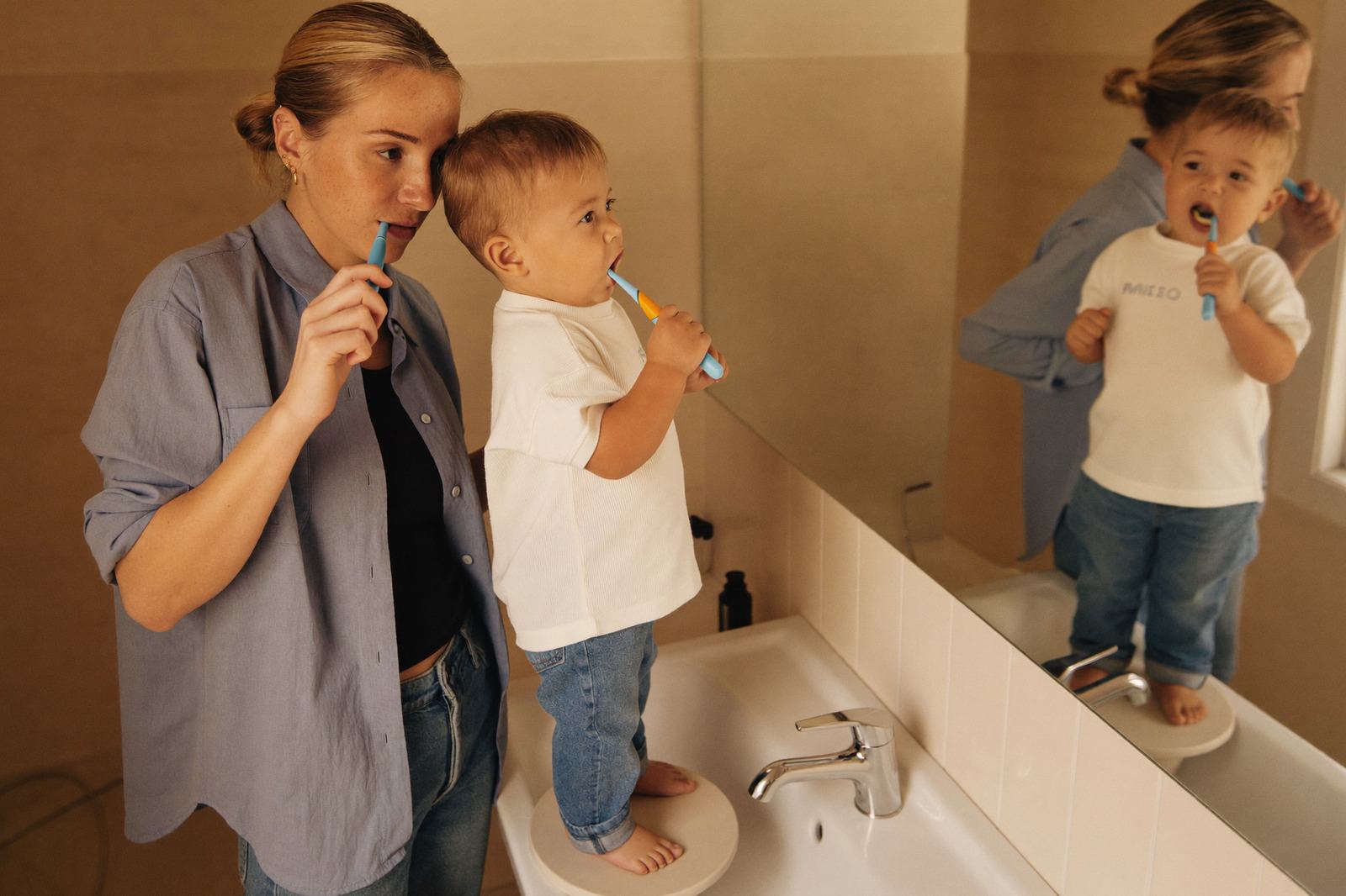 Mamá cepillando los dientes de su hijo pequeño frente al lavabo del baño