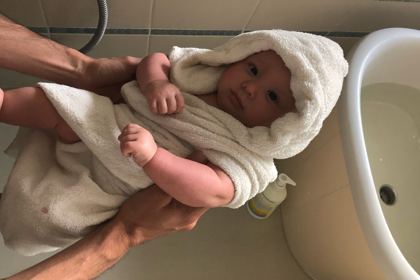 Bebé en la tina de baño con agua poco profunda, jugando con las manos