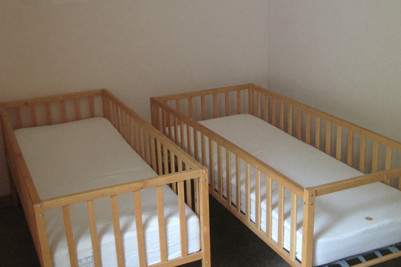 Dos cunas individuales con colchón firme y sin objetos, en una sala de cuidado infantil