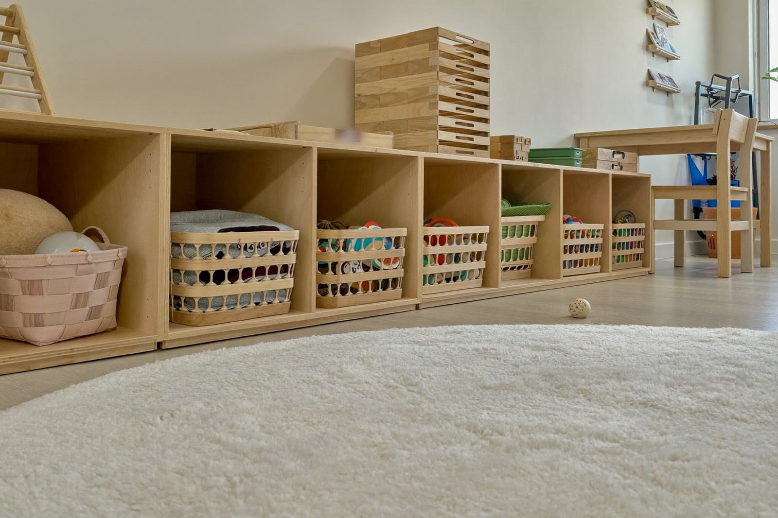 Sala de cuidado infantil con un tapete amplio y juguetes ordenados en canastas sobre repisas bajas