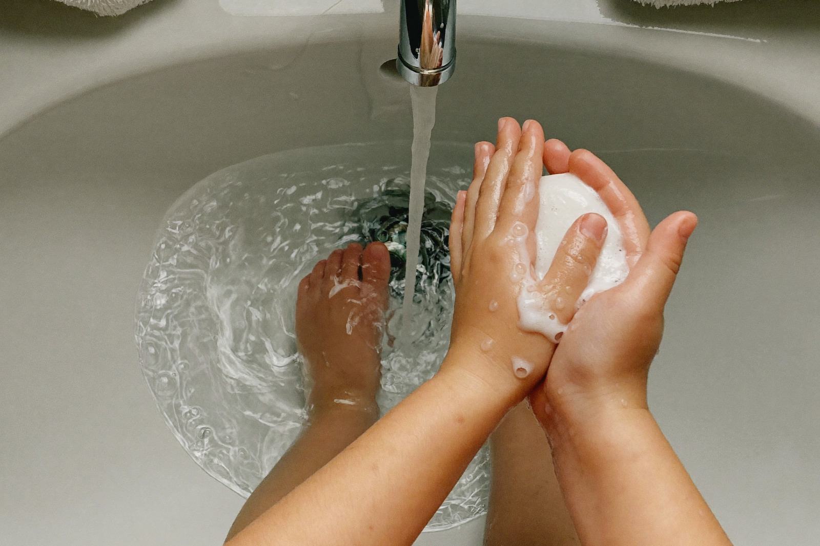 Manos de un niño pequeño enjabonándose bajo el chorro de agua de un lavabo