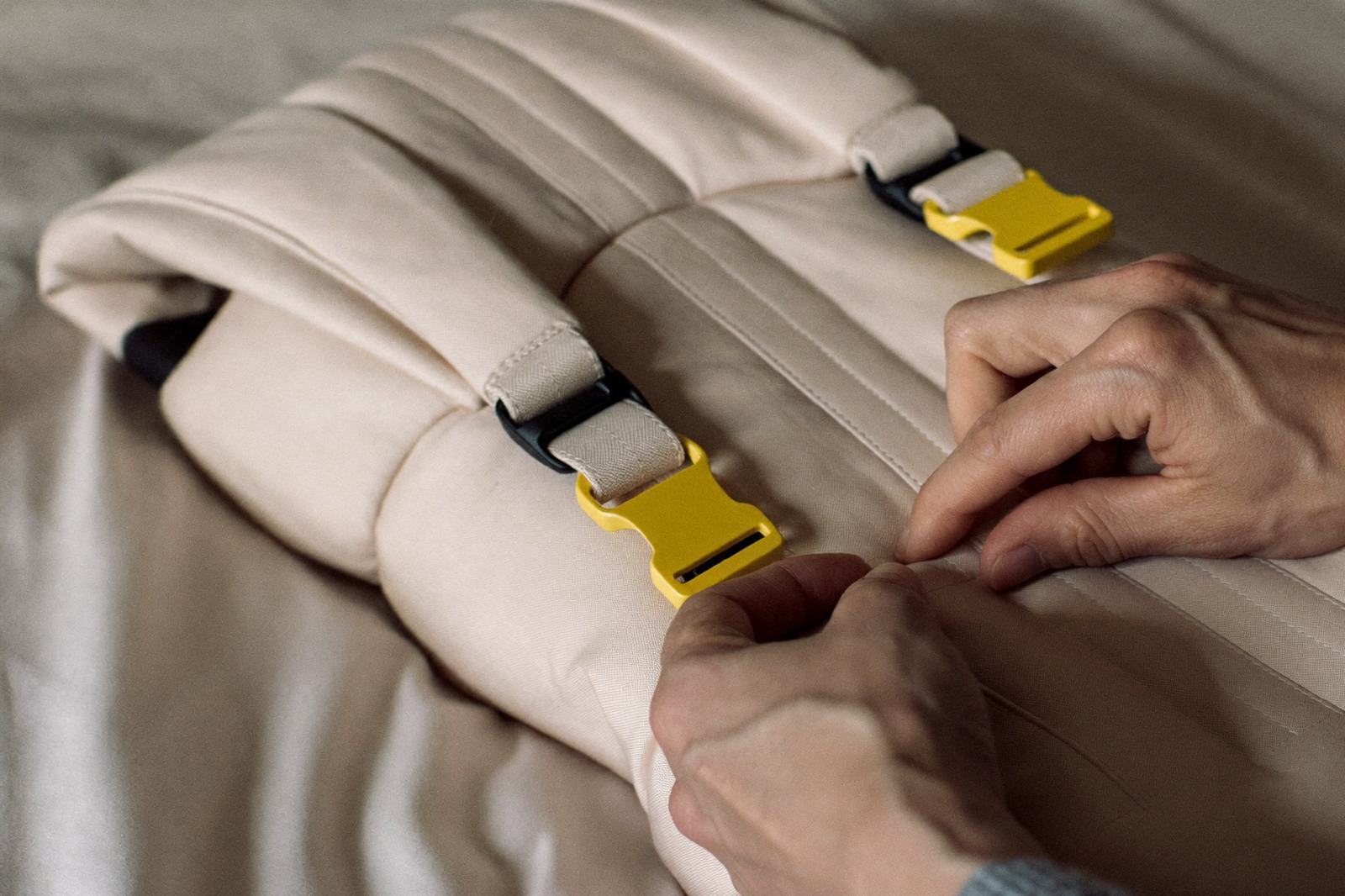 Manos revisando las costuras y las hebillas de un portabebés de tela extendido sobre una cama