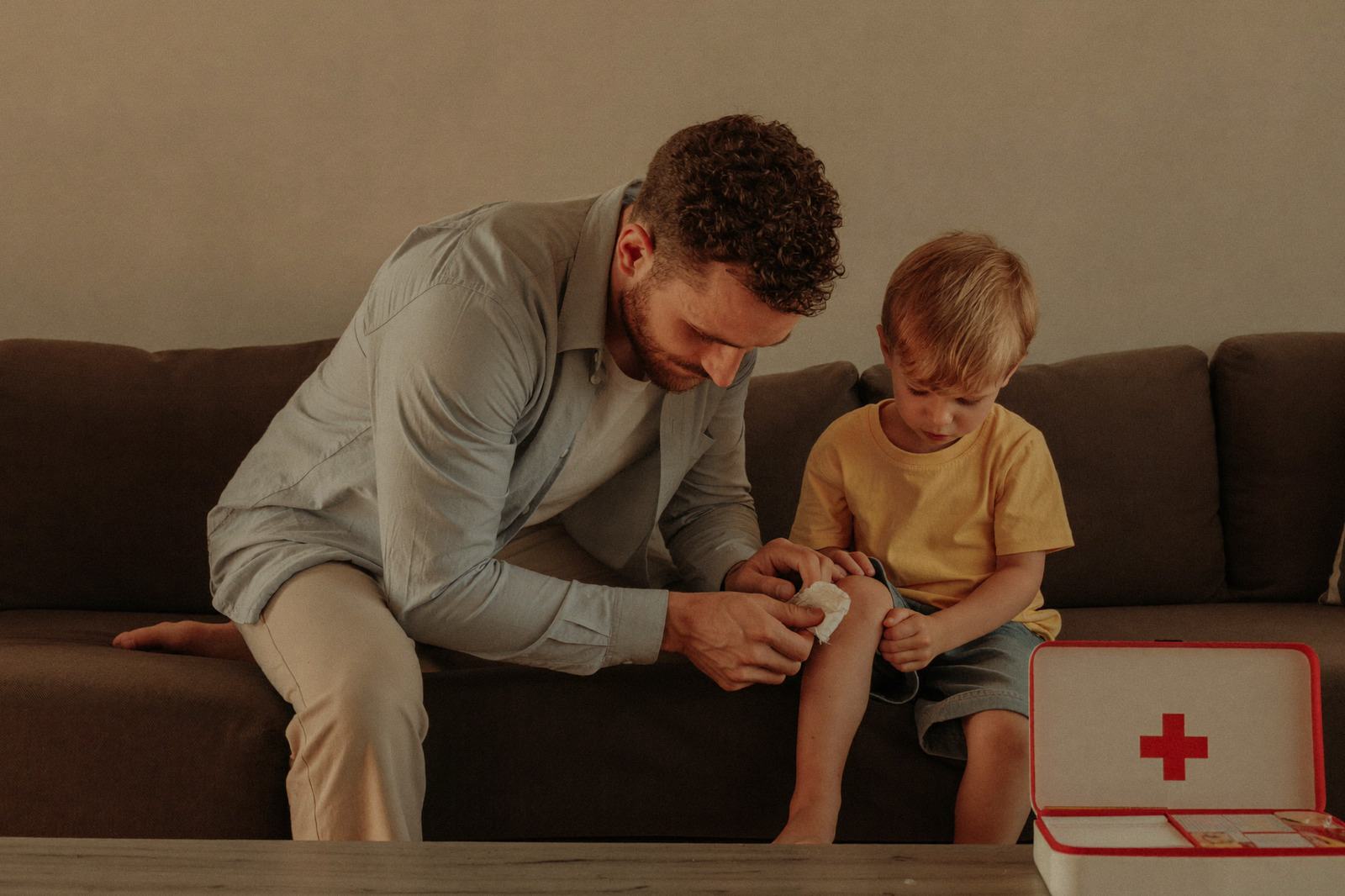 Papá curando la rodilla raspada de su hijo pequeño sentado en el sillón de la sala