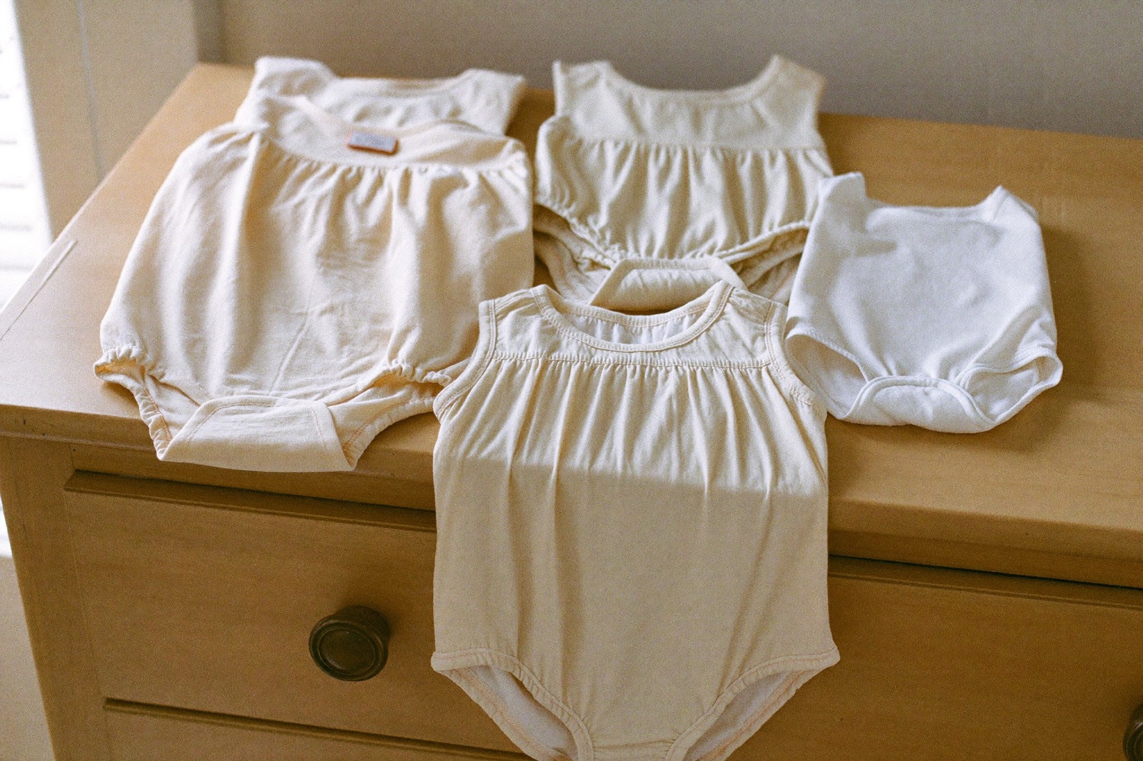 Mamelucos y camisetas de bebé de algodón doblados sobre una cómoda de madera clara