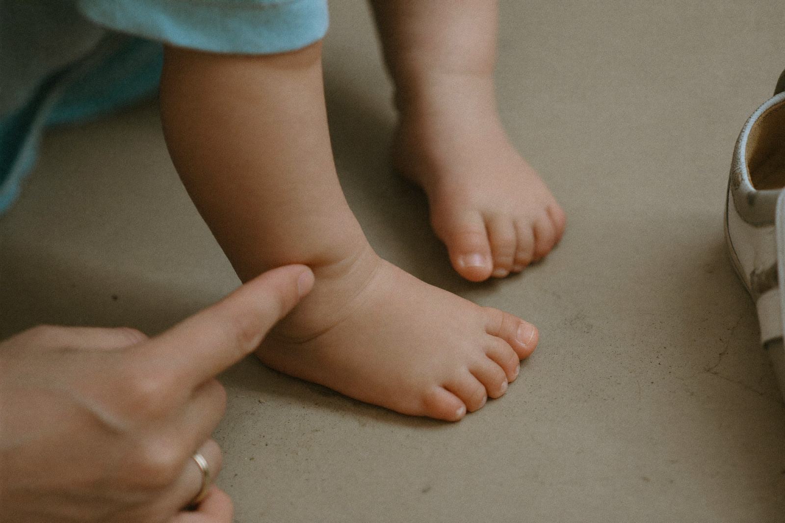 Mano de un adulto revisando con el dedo el pie descalzo de un niño pequeño